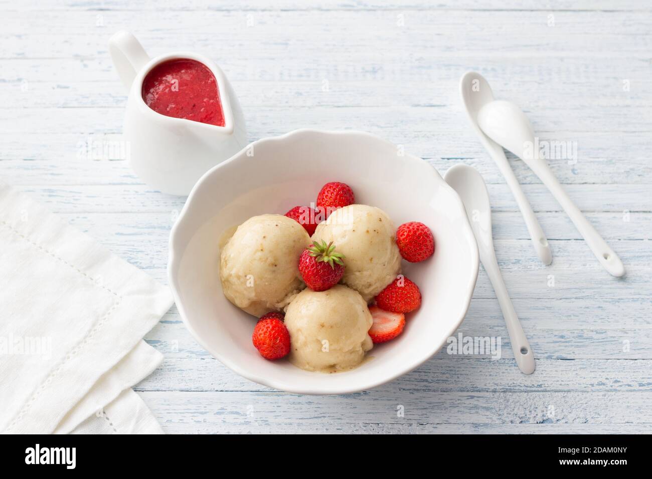 Vegan banana ice cream with strawberry sauce and fresh strawberries in a white bowl on a light blue wooden background Stock Photo