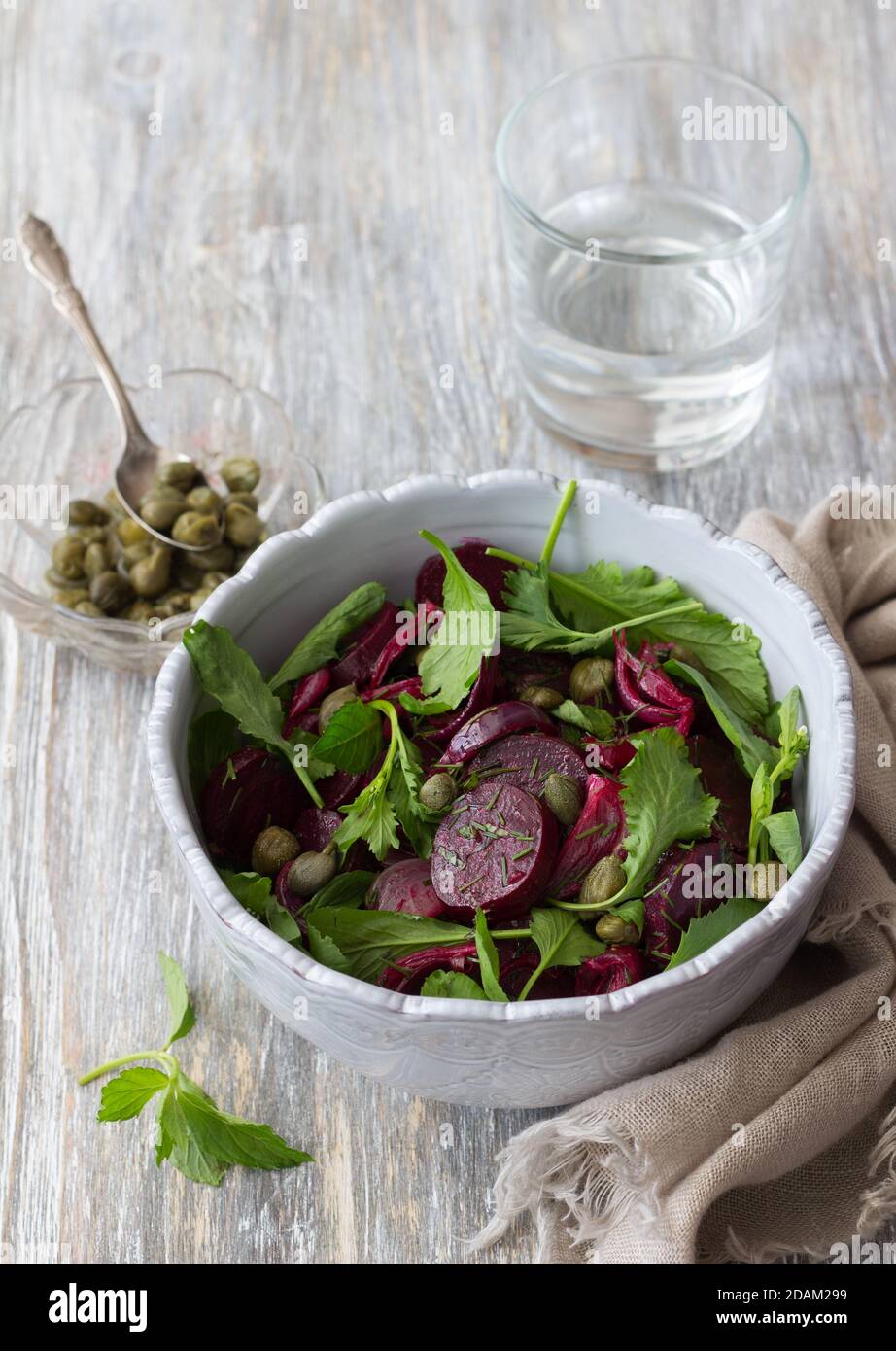 Beetroot salad with baked red onion, capers, watercress, greens and vinaigrette sauce. Vegan healthy food. In a blue bowl on a wooden table Stock Photo