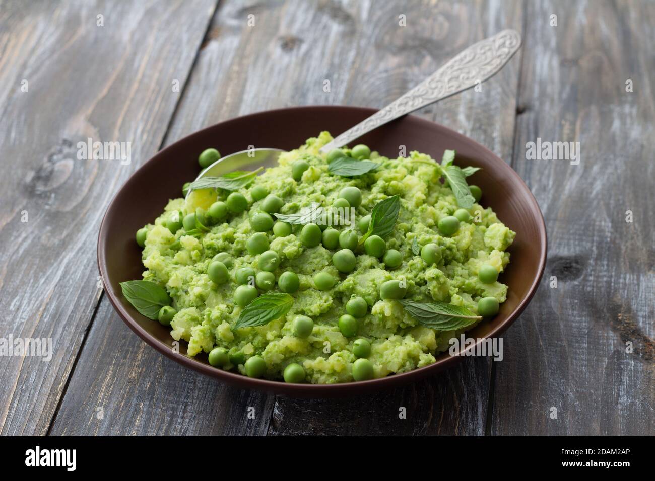 Mashed potatoes with green peas, mint and olive oil in a ceramic bowl on a wooden table. Healthy vegetarian food Stock Photo