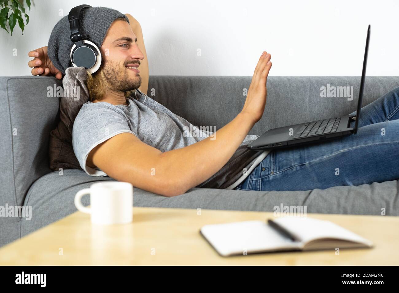 Handsome young business caucasian man working at home using laptop and talking with mobile phone saying hello Stock Photo