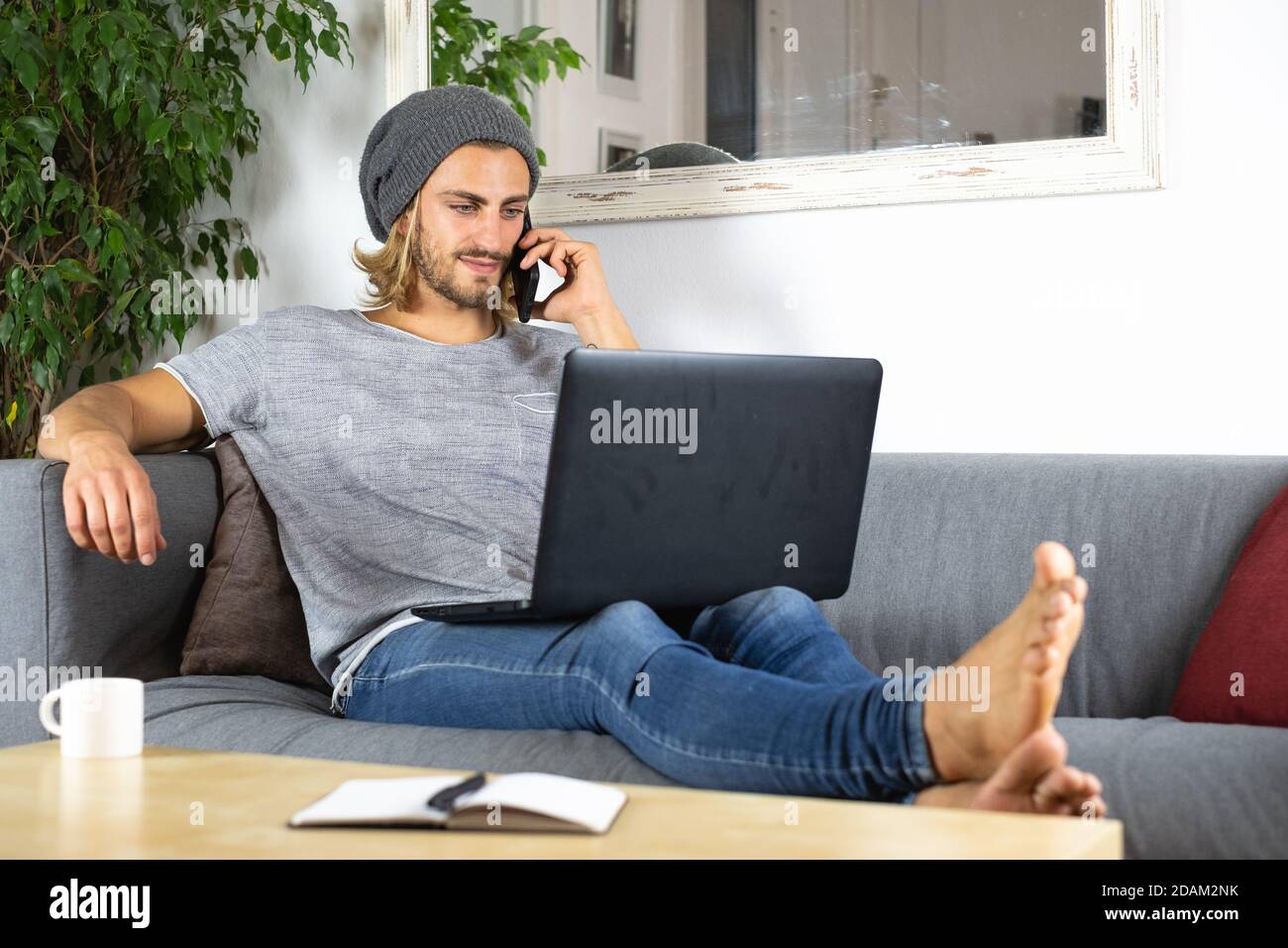 Handsome young business caucasian man working at home using laptop and talking with mobile phone Stock Photo