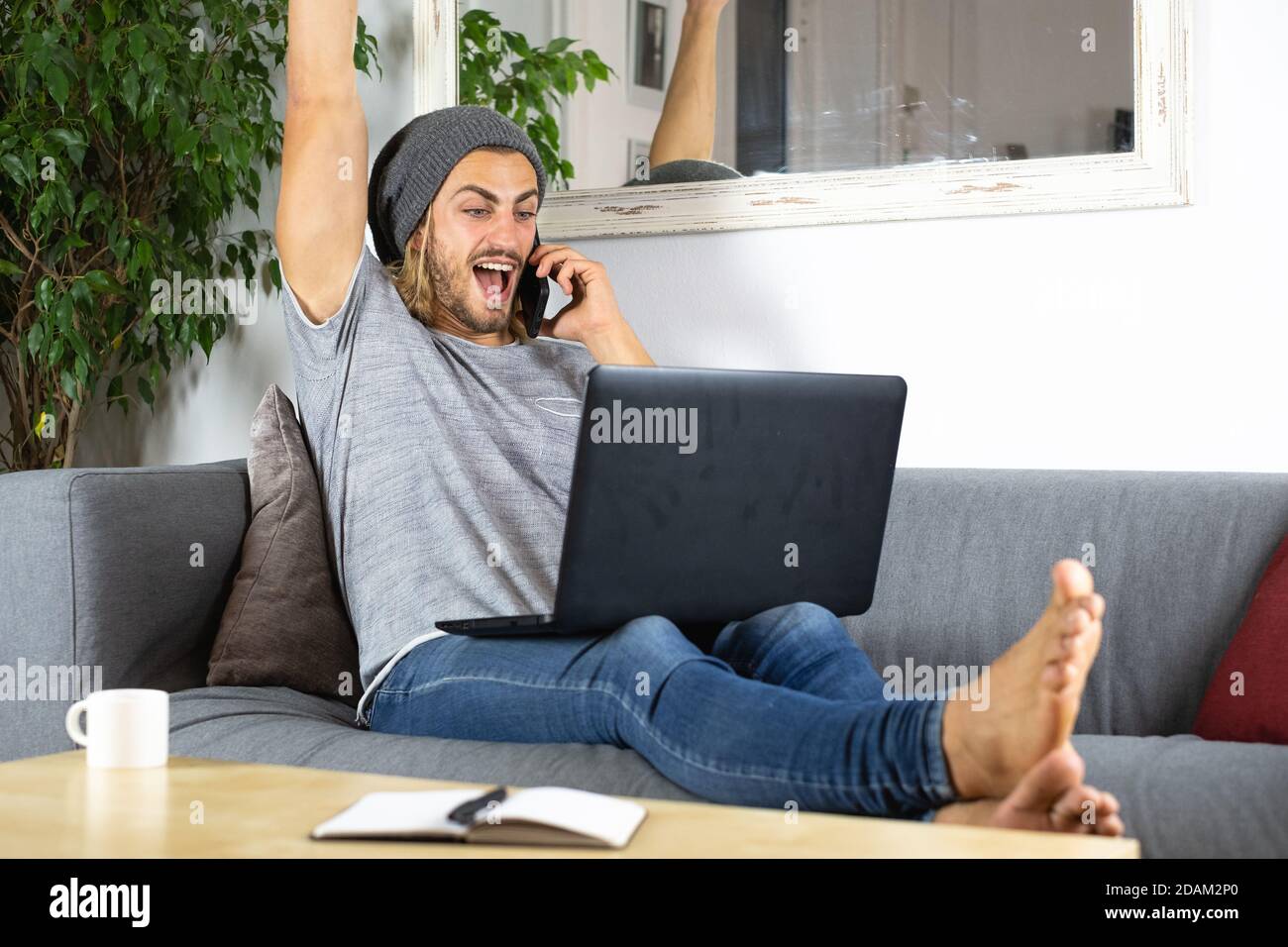 Handsome young business caucasian man working at home using laptop and talking with mobile phone feeling happy Stock Photo
