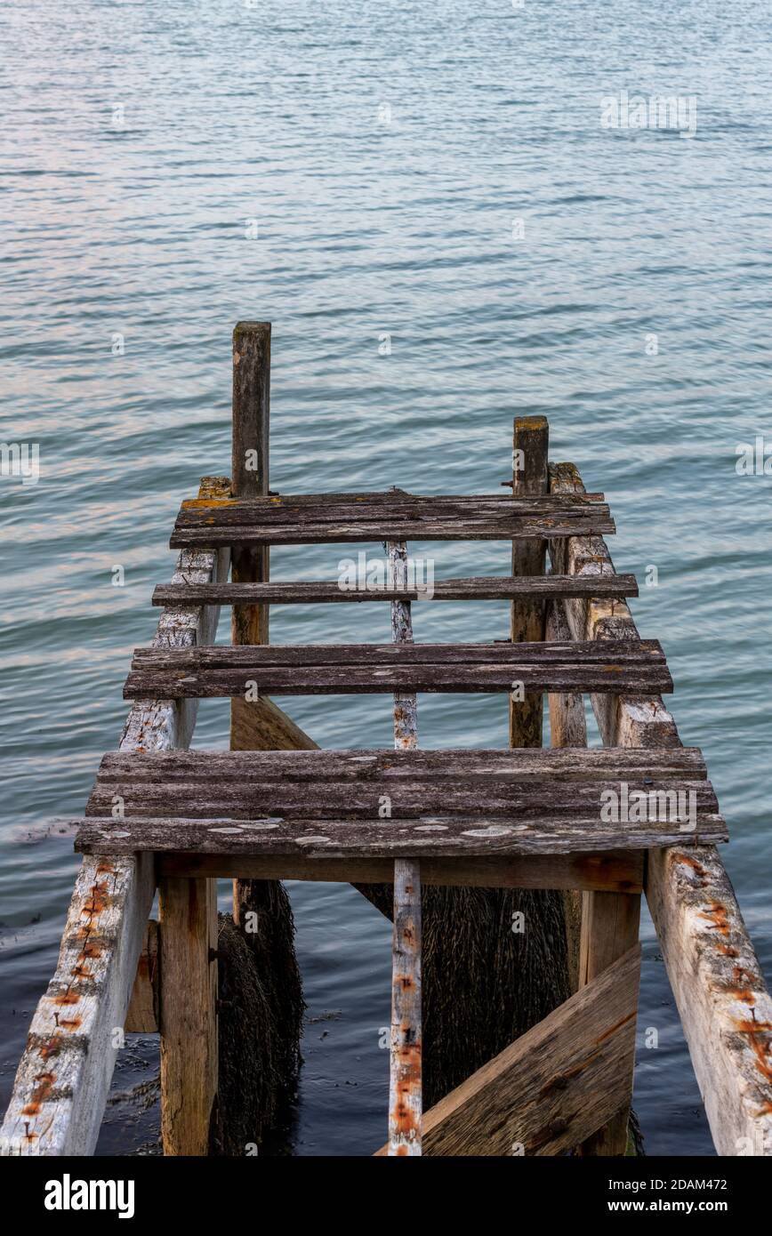 n old rickety rotten wooden jetty or pier used as a landing stage for small boats at the seaside in yarmouth on the isle of wight. Stock Photo