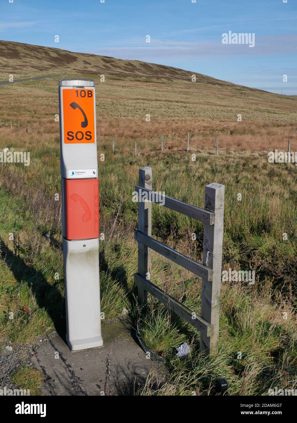 Moorland SOS telephone post grey with two orange red signs with black letters and depiction of phone on moorland small wood fence to side Stock Photo