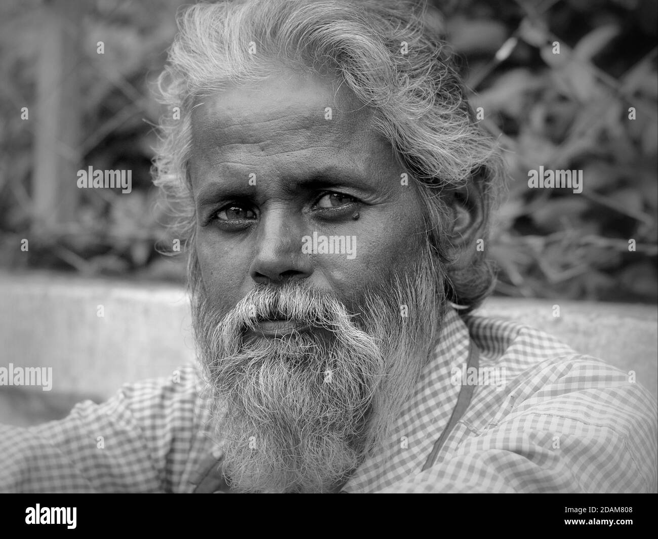 Middle-aged Indian migrant labourer with full beard sits by the roadside, waits for a daily job and poses for the camera. Stock Photo