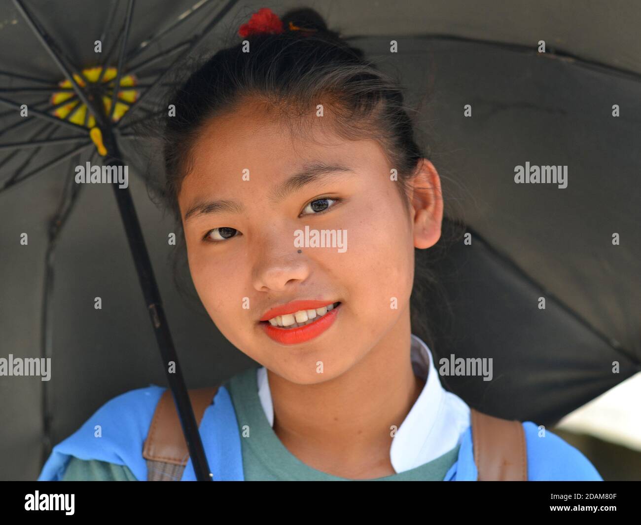 Pretty Northeast Indian Apatani female high school student with red lipstick smiles for the camera under her black sun umbrella. Stock Photo