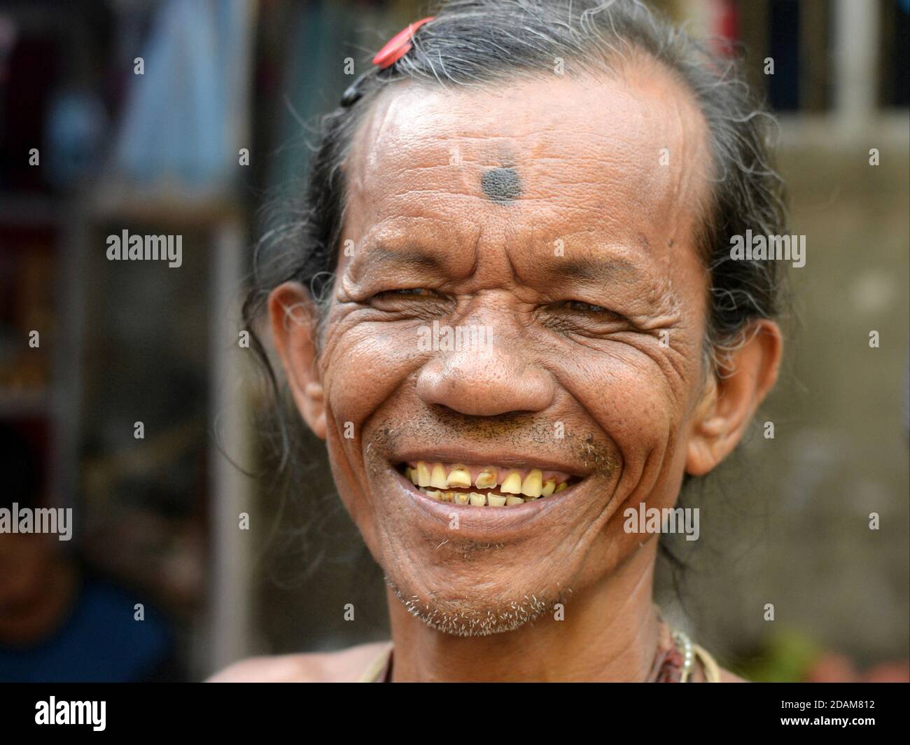 Laughing Indian Hindu male devotee with red hairclip and tattooed third eye on his forehead looks with narrowed eyes at camera. Stock Photo
