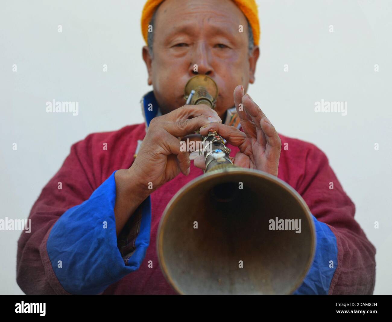 Elderly Northeast Indian trumpeter wears Tibetan Buddhist outfit and plays his traditional Tibetan trumpet (gyaling, dungchen, Buddhist prayer horn). Stock Photo