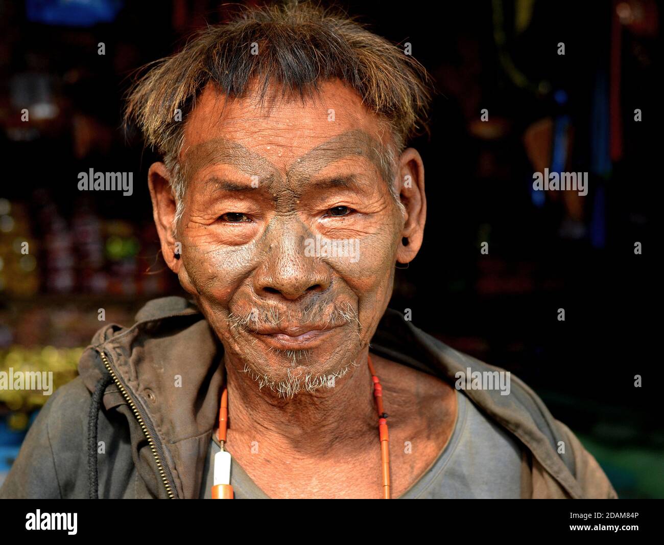 Old retired Indian Konyak Naga warrior and headhunter with distinctive tribal facial tattoo and traditional hairstyle poses for the camera. Stock Photo