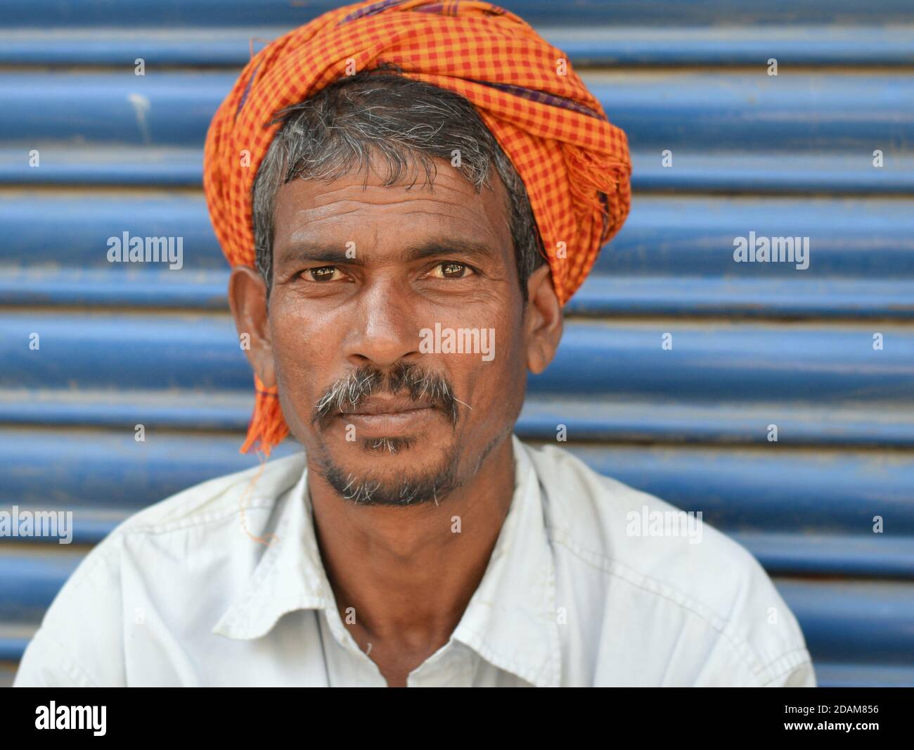 Indian migrant labourer wears an orange-checkered turban-like head wrap and poses for the camera. Stock Photo