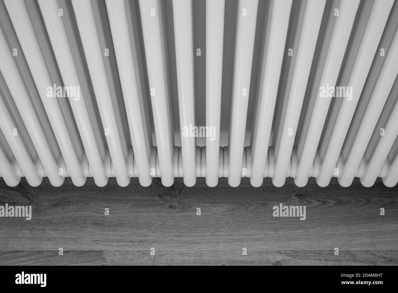 Black and white image of a radiator pipes over parquet floor Stock Photo
