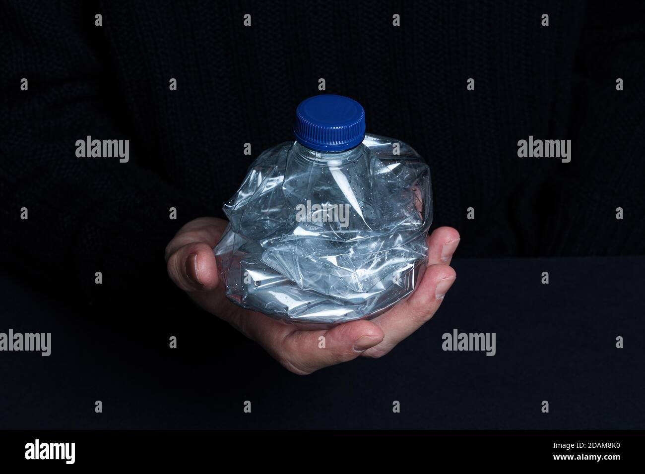 Hand holding smashed empty plastic bottle isolated on a black background Stock Photo