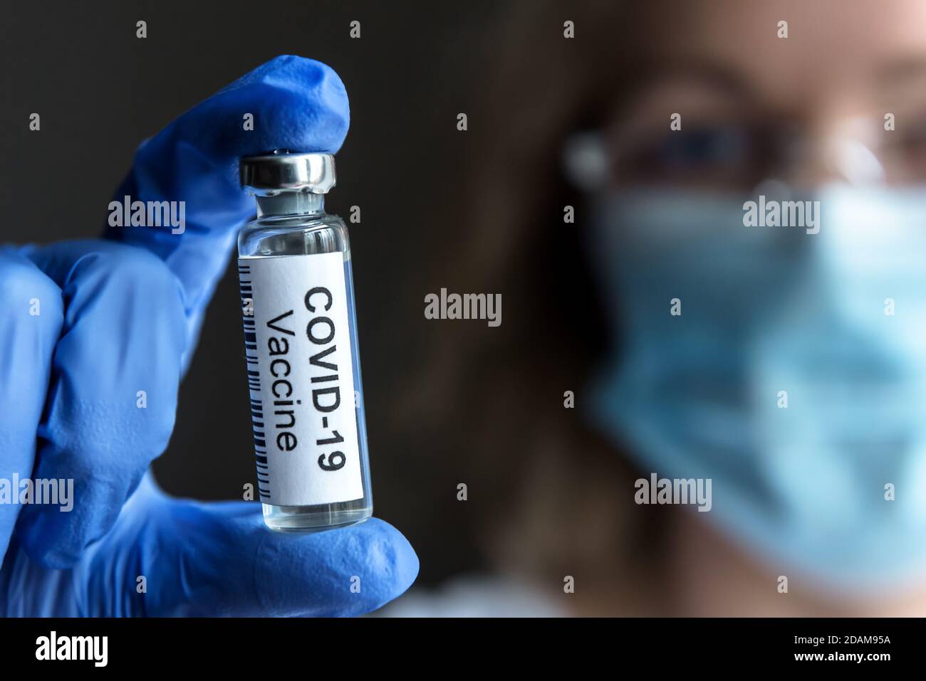 COVID-19 vaccine in doctor hand close-up, female researcher with mask and bottle with vaccine for coronavirus cure in laboratory. Concept clinical tri Stock Photo