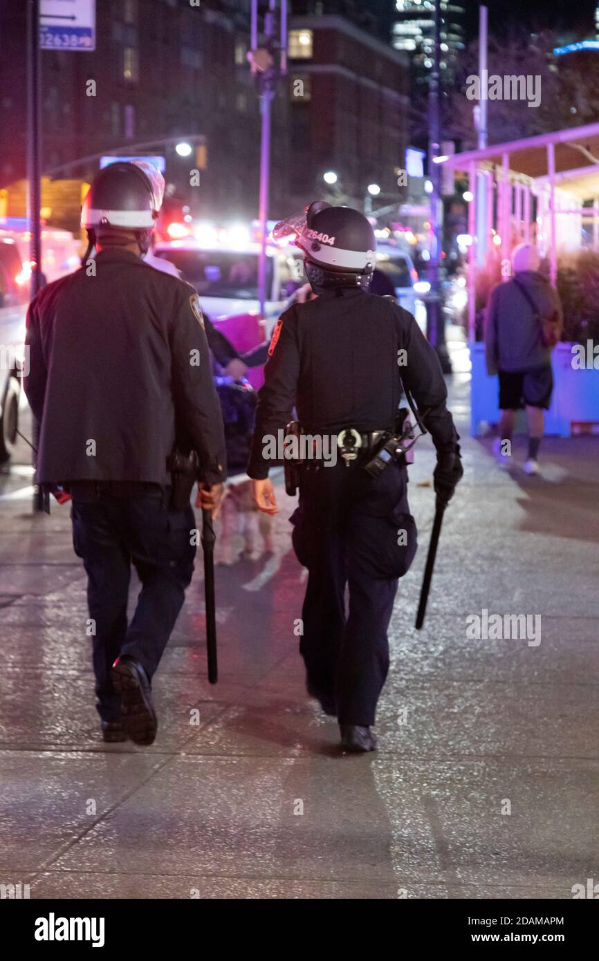 Rear View of Two Heavily Geared NYPD Officers walking with Helmets and Baton swinging, Lens Flare, Greenwich Village, New York City, New York, USA Stock Photo