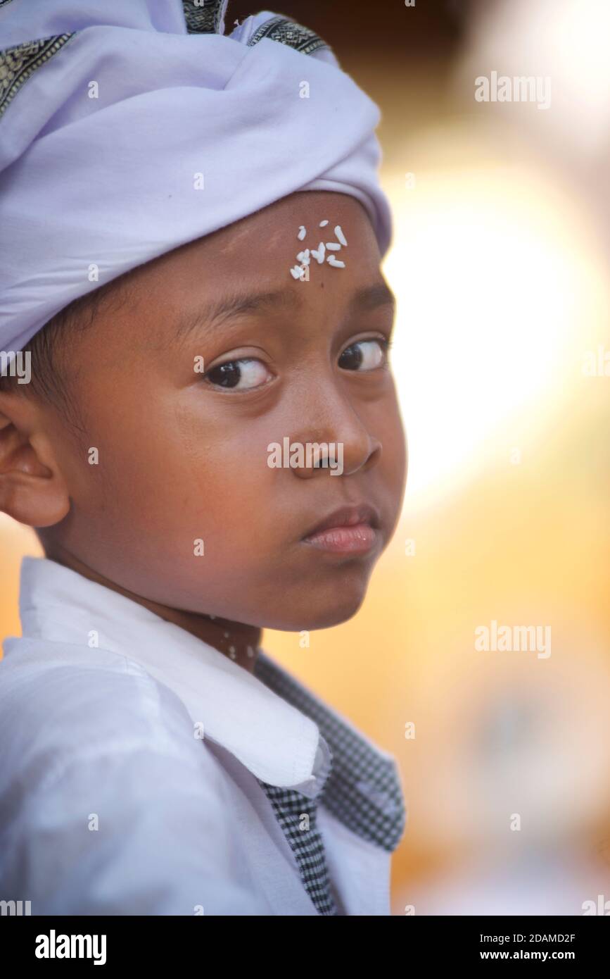 Portrait of a Balinese boy in traditional white attire with rice on his ceremonial forehead
