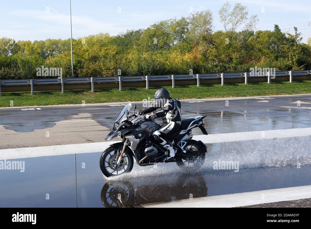 Rider doing aquaplaning or hydroplaning tests on a motorbike speeding along a wet road to see when the tyres will start to loose contact with the surf Stock Photo