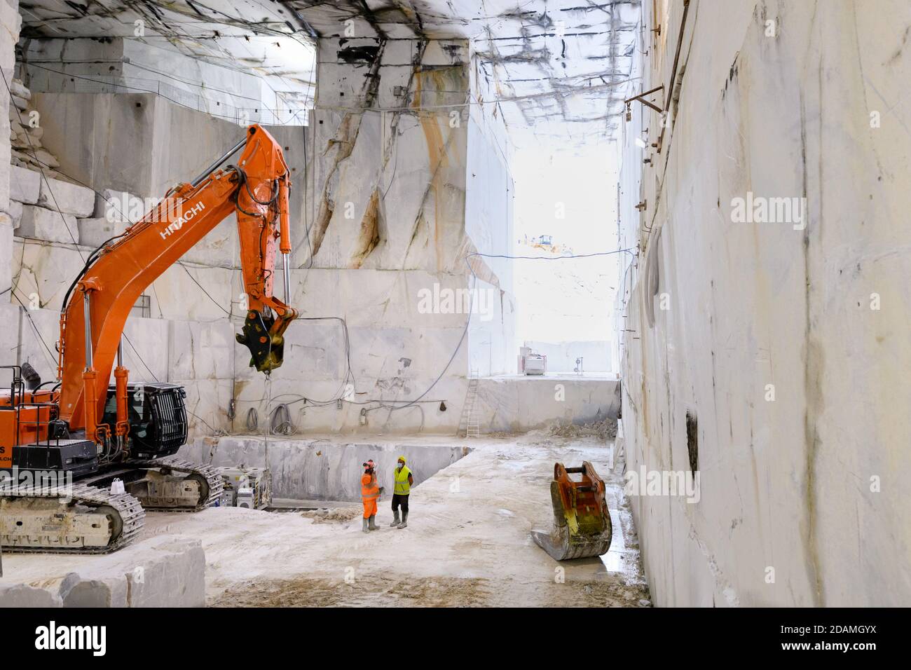 Workers and heavy duty equipment inside an open cast Carrara marble quarry in Tuscany Italy with a view down a cut rock face inside a mountain Stock Photo