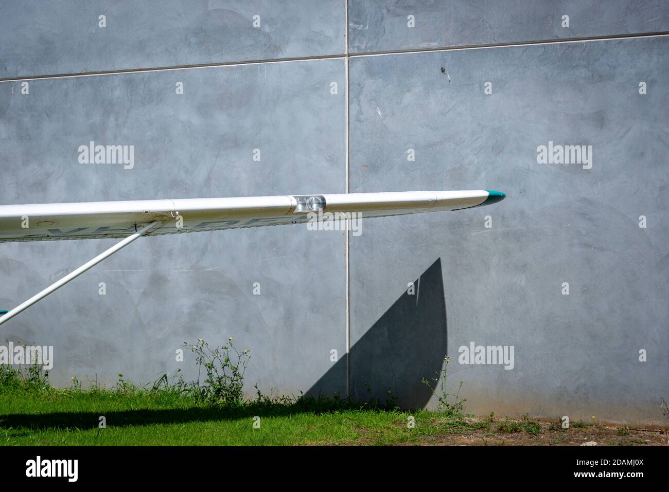 Wing of an old plane, throwing a shadow against a concrete wall and green lawn Stock Photo