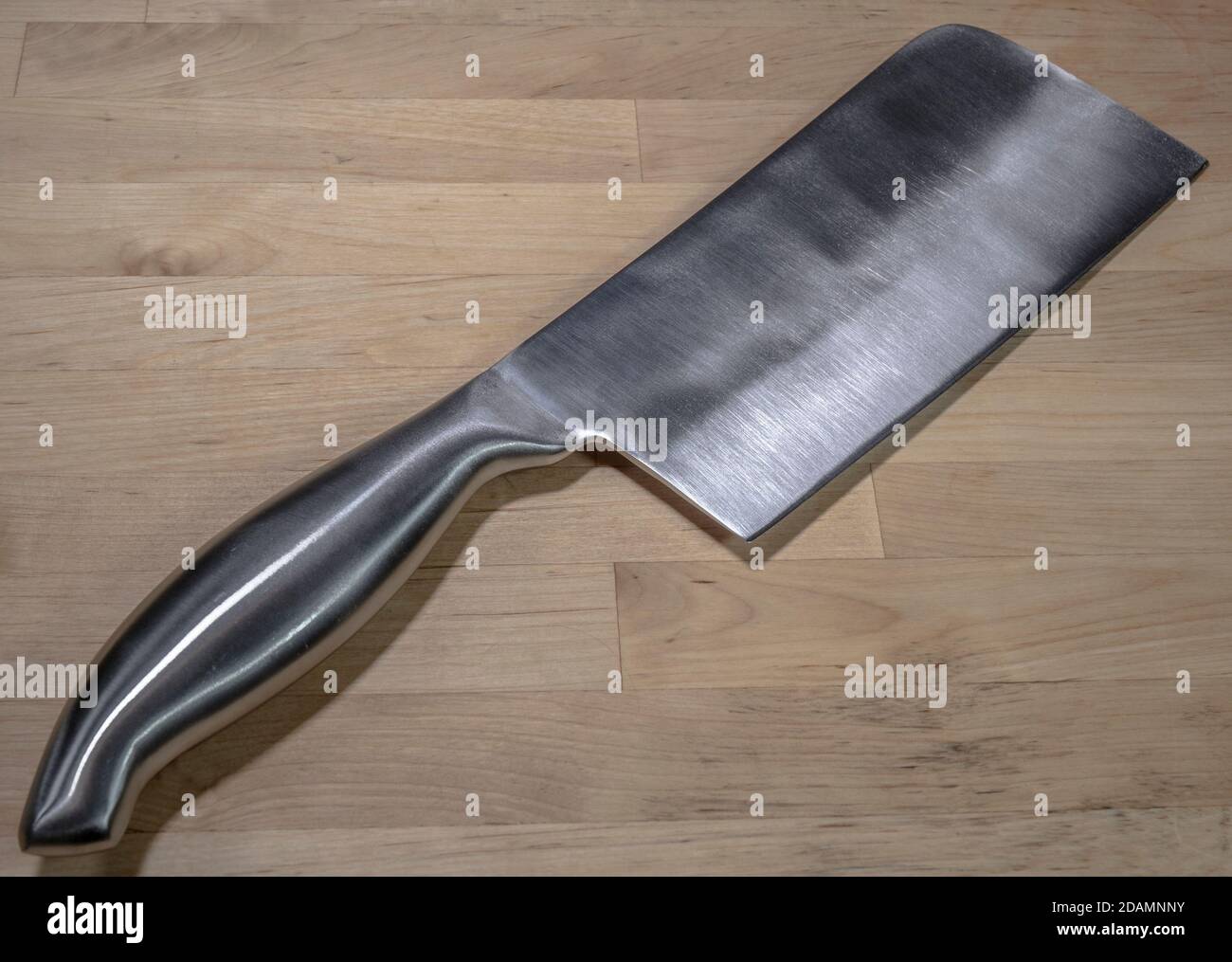 Closeup POV shot of a professional stainless steel cleaver lying on one side on a wooden table. Stock Photo