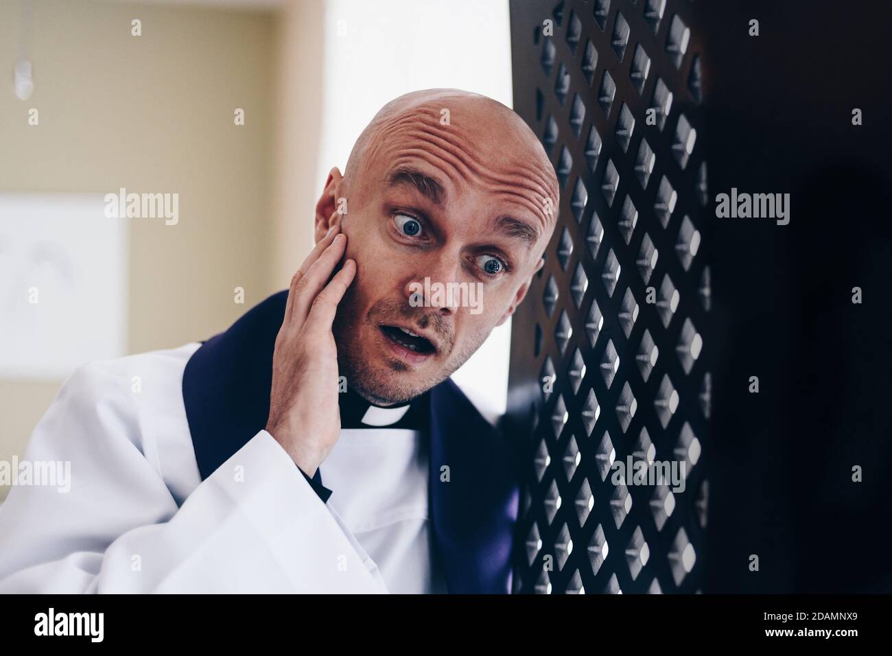 Surprised vicar priest in the confession booth Stock Photo