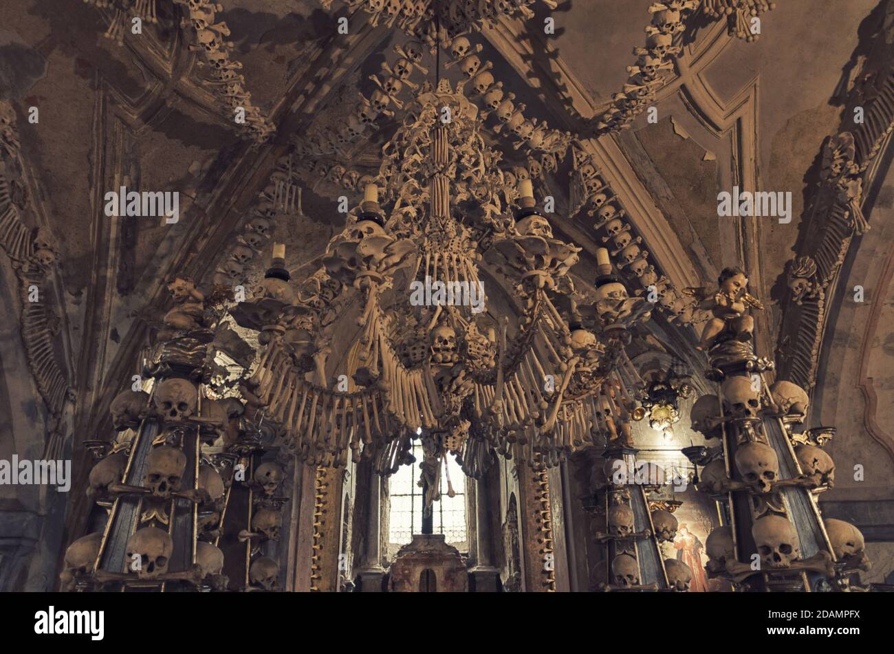 Kutna Hora, Czech Republic, May 14, 2019: Room with colonnade of human  bones and skulls. Bony lustre hang rom ceiling. Altar with crucifixion of  Jesus Christ in Kostnice Church in Kutna Hora
