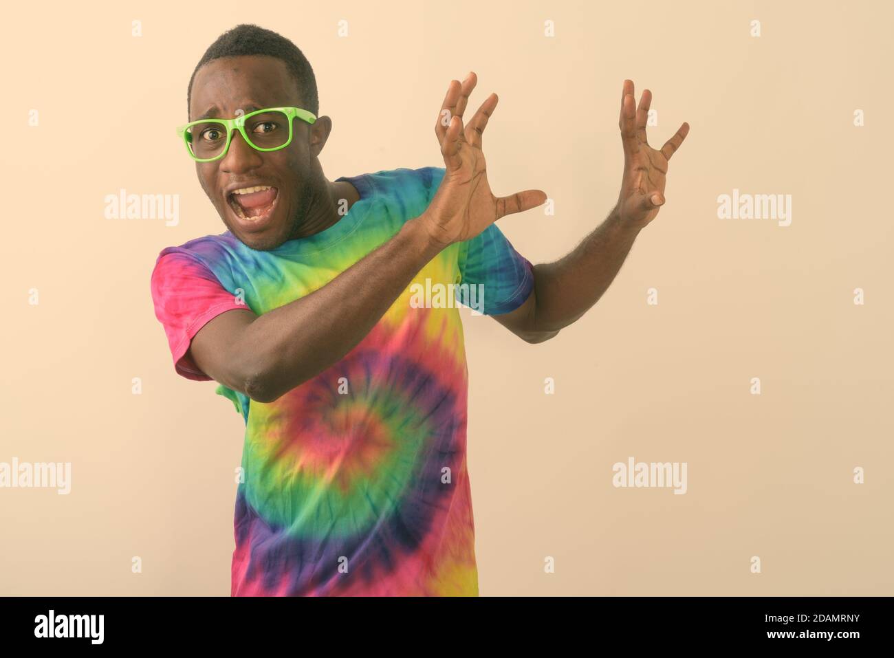 Studio shot of young scared black African man looking afraid and raising his arms against white background Stock Photo