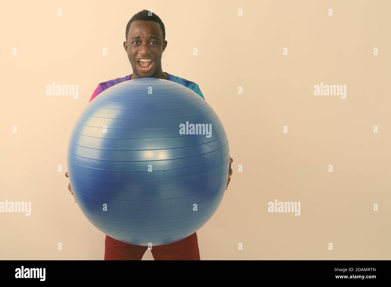 Studio shot of young black African man holding big exercise ball ready for gym against white background Stock Photo