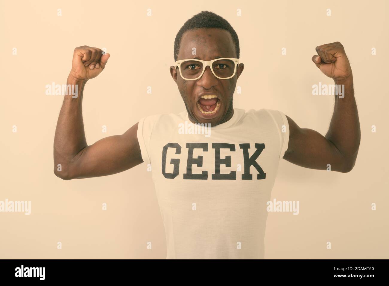 Studio shot of young black African nerd man wearing Geek shirt while flexing his arms and showing bicep muscles against white background Stock Photo