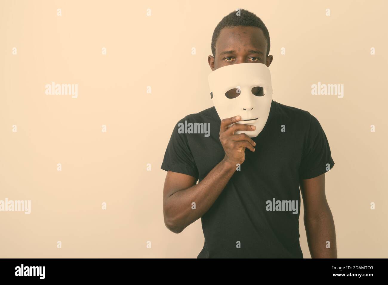 Studio shot of young black African man holding mask in front of his face Stock Photo