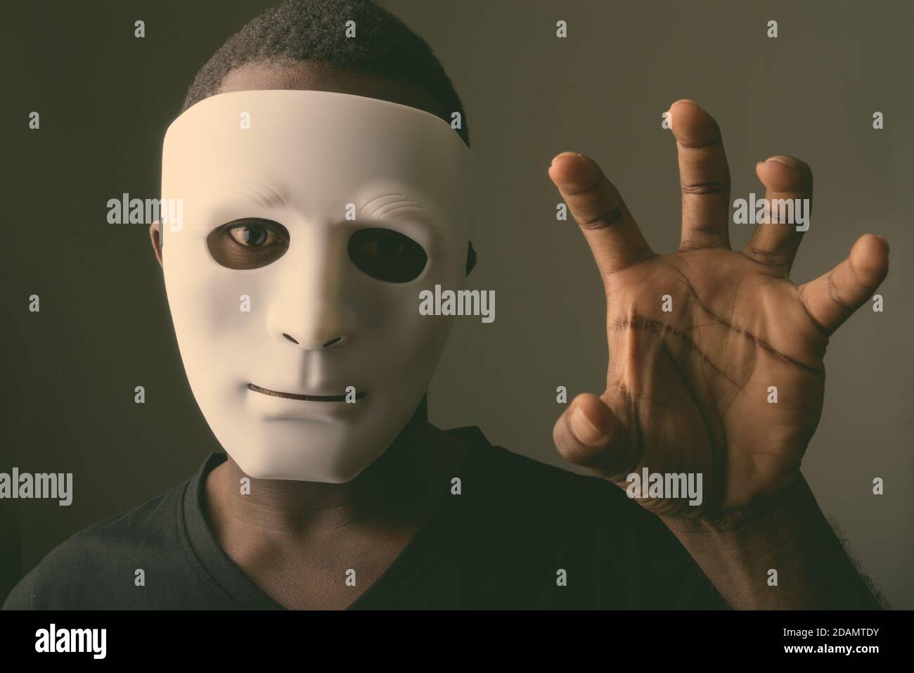 Studio shot of young black African man in dark room wearing mask and showing his hand Stock Photo