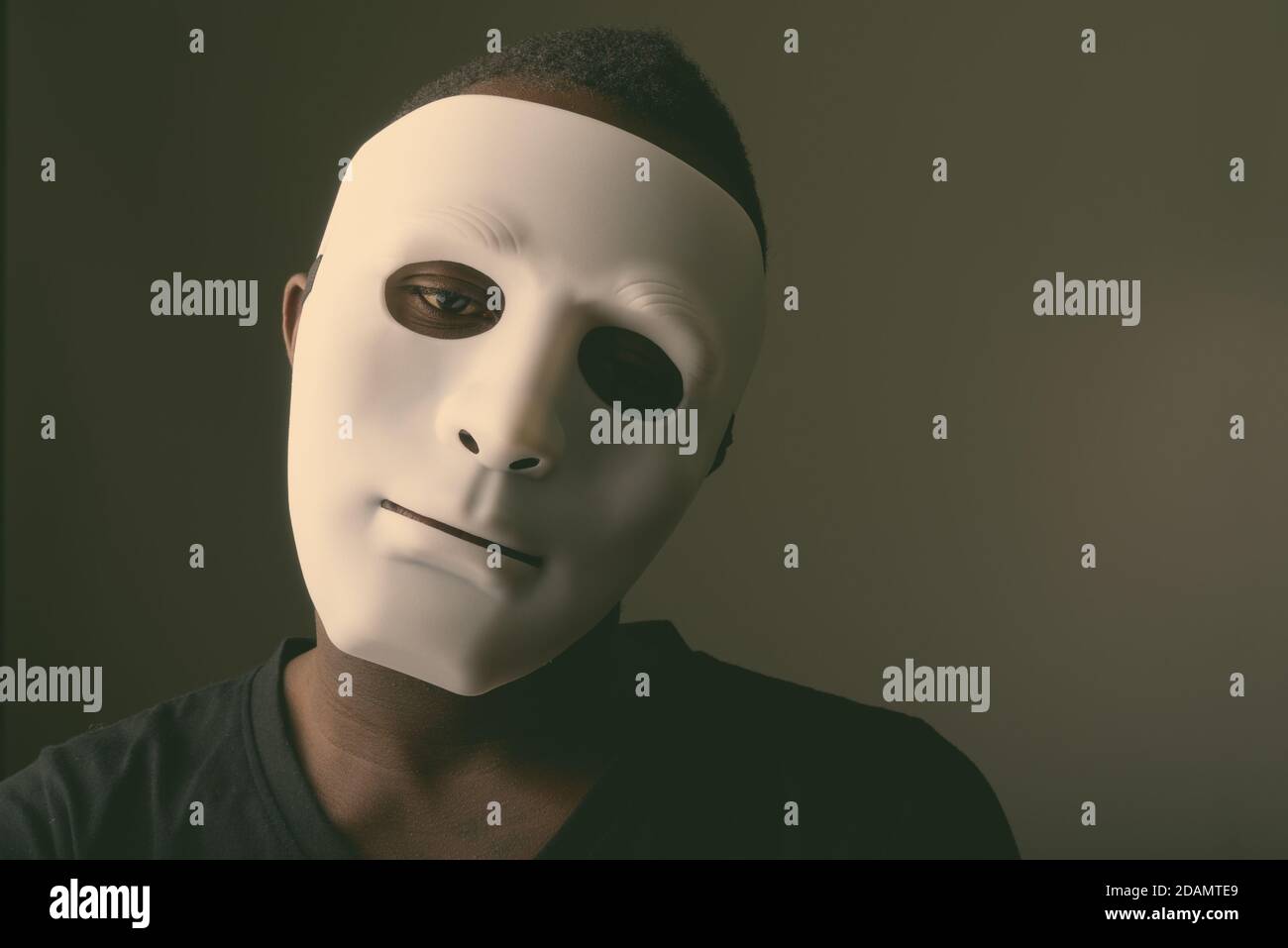 Studio shot of young black African man in dark room wearing mask Stock Photo