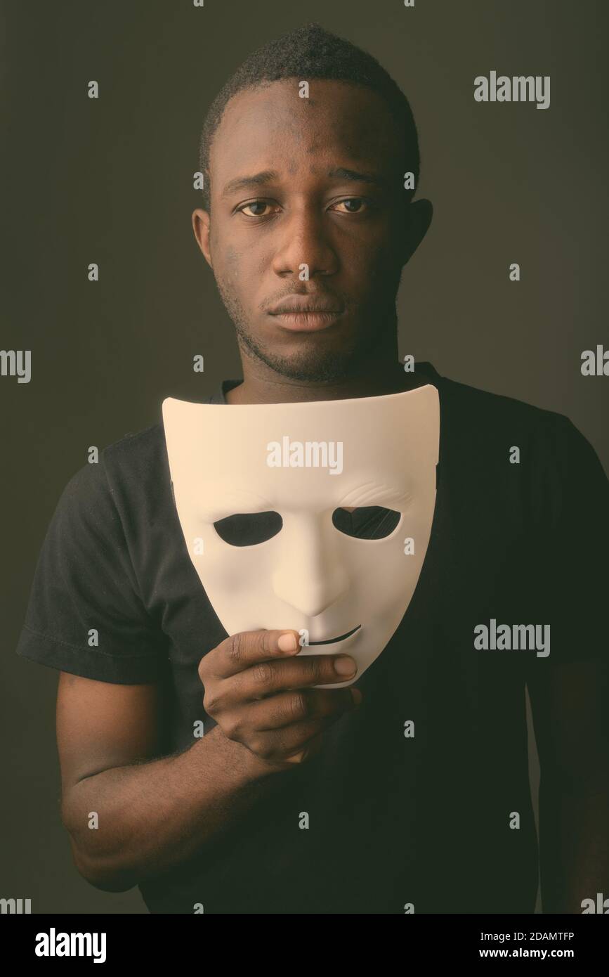 Studio shot of young black African man in dark room holding mask Stock Photo