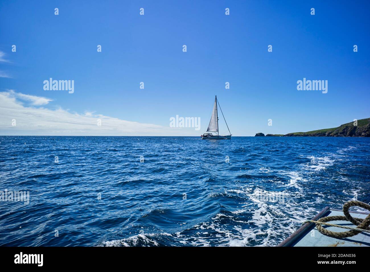 A sailing yacht heads for the channel between the Calf of Man and the main Isle of Man island at high tide Stock Photo