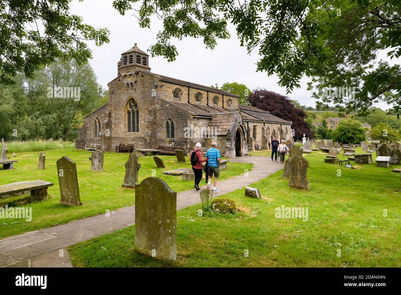 Historic scenic St Michael & All Angels Church exterior & people walking on churchyard pathway to entrance porch - Linton, Yorkshire Dales, England UK Stock Photo