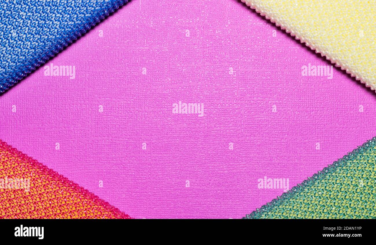 Colorful cleaning sponges placed in corners, diamond shape borders on plain pink background with copy space. Stock Photo