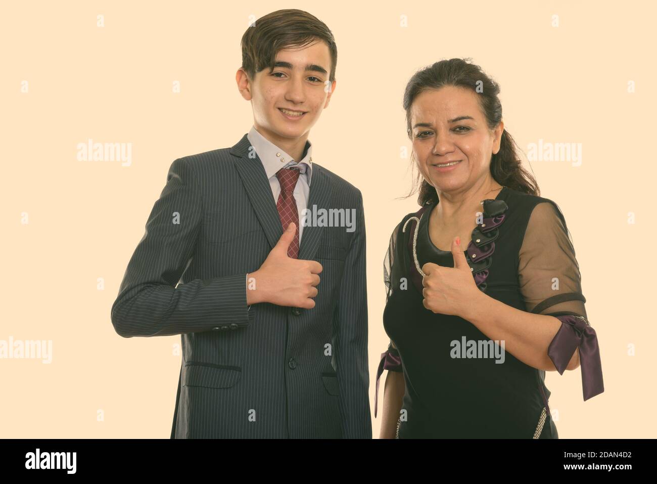 Studio shot of happy young Persian teenage businessman and mature Persian woman smiling while giving thumb up together Stock Photo