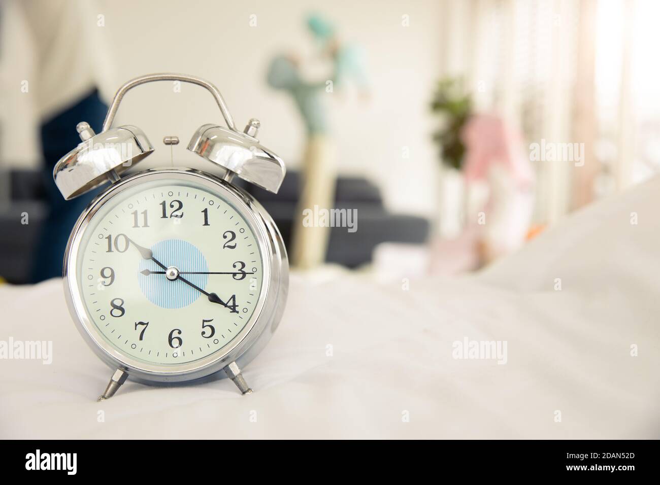 family time with new baby concept, clock with blur mother play with newborn infant at home background. Stock Photo