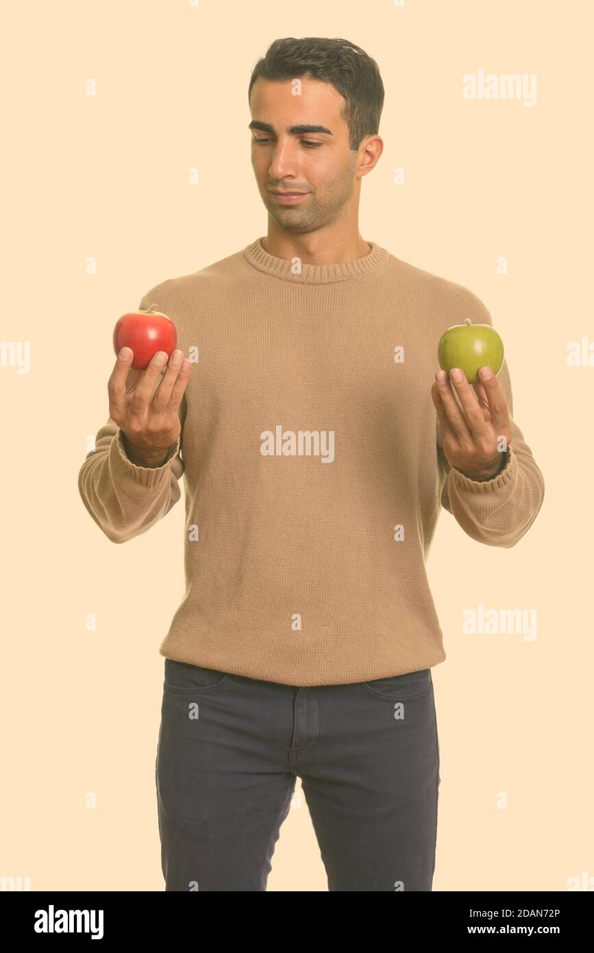 Young handsome Iranian man choosing between red and green apple Stock Photo