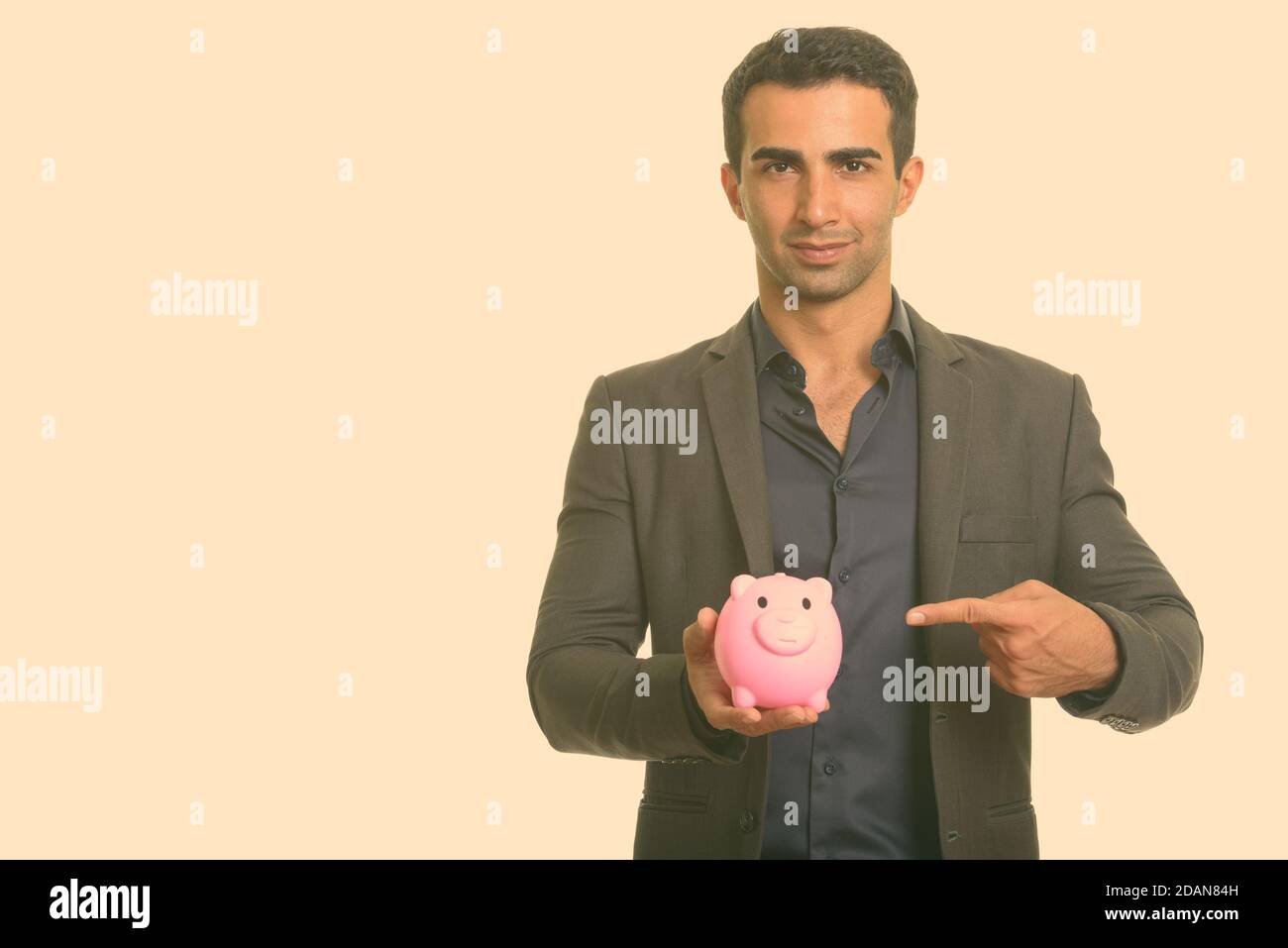 Young handsome Iranian businessman holding piggy bank while pointing ...