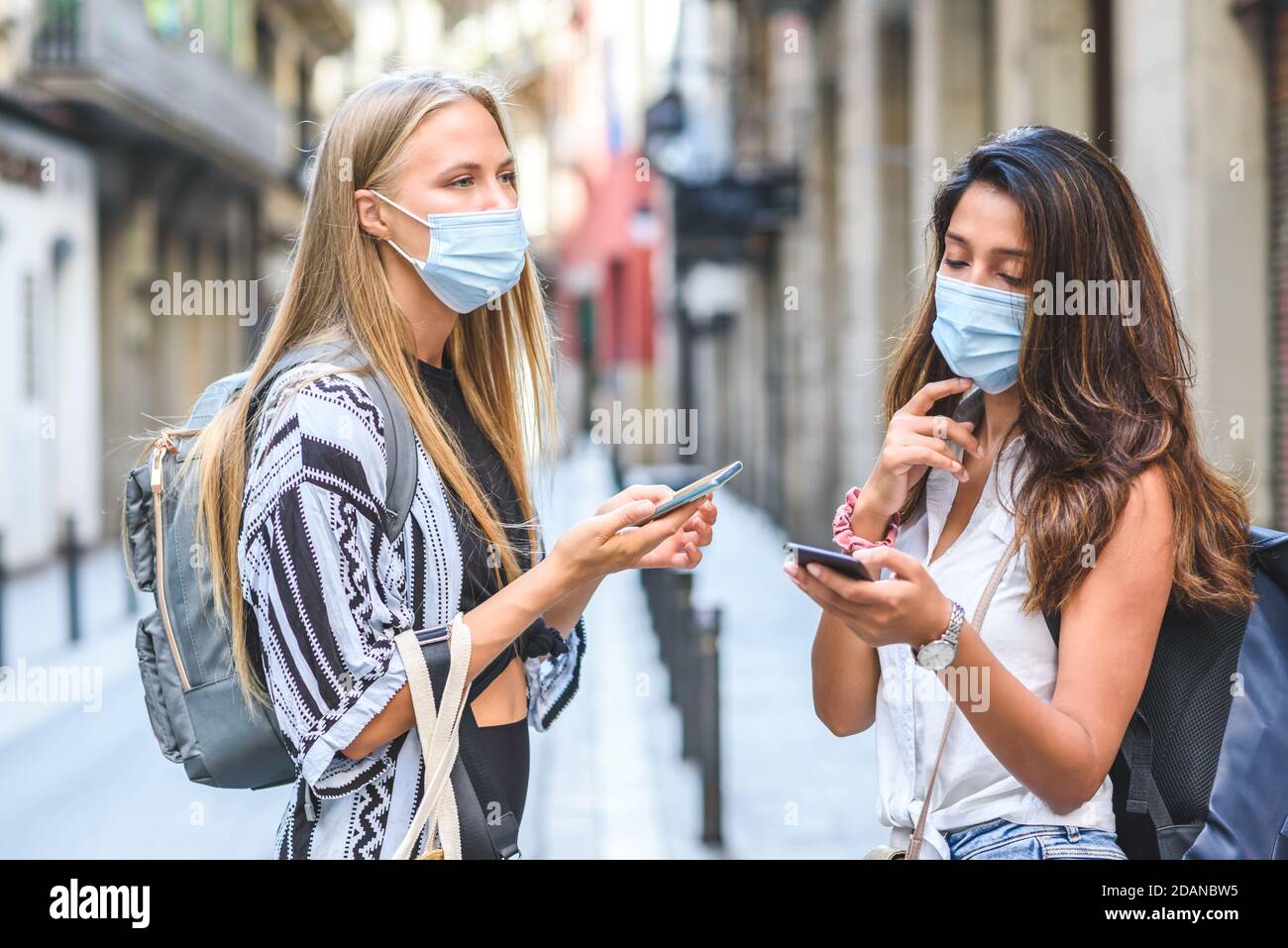 asian and caucasian female travelers with backpacks on the street and looking for information on their phones Stock Photo