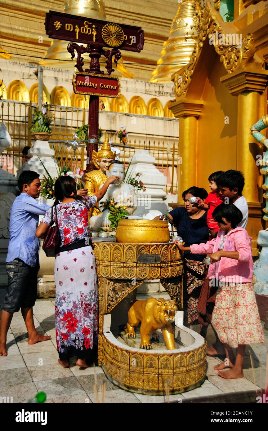 A Burmese family pour water on the Buddha statue at the Monday shrine at the Shwedagon Pagoda Yangon Myanmar Stock Photo
