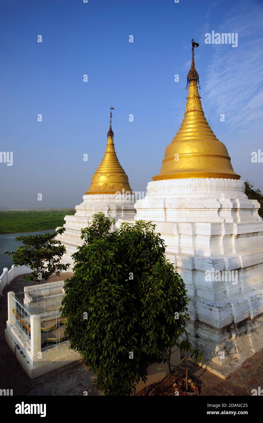 Two gold topped Burmese temple stupas on the banks of the Ayeyarwady river looking across to Sagaing near Mandalay Myanmar Stock Photo