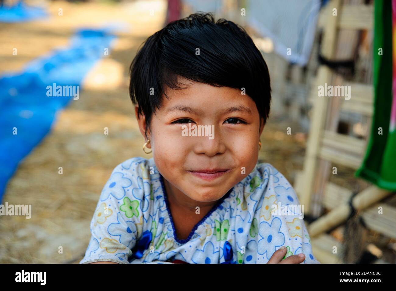 A portrait of a happy smiling young Burmese girl with fishing nets laid out in the background on Ngapali beach Stock Photo
