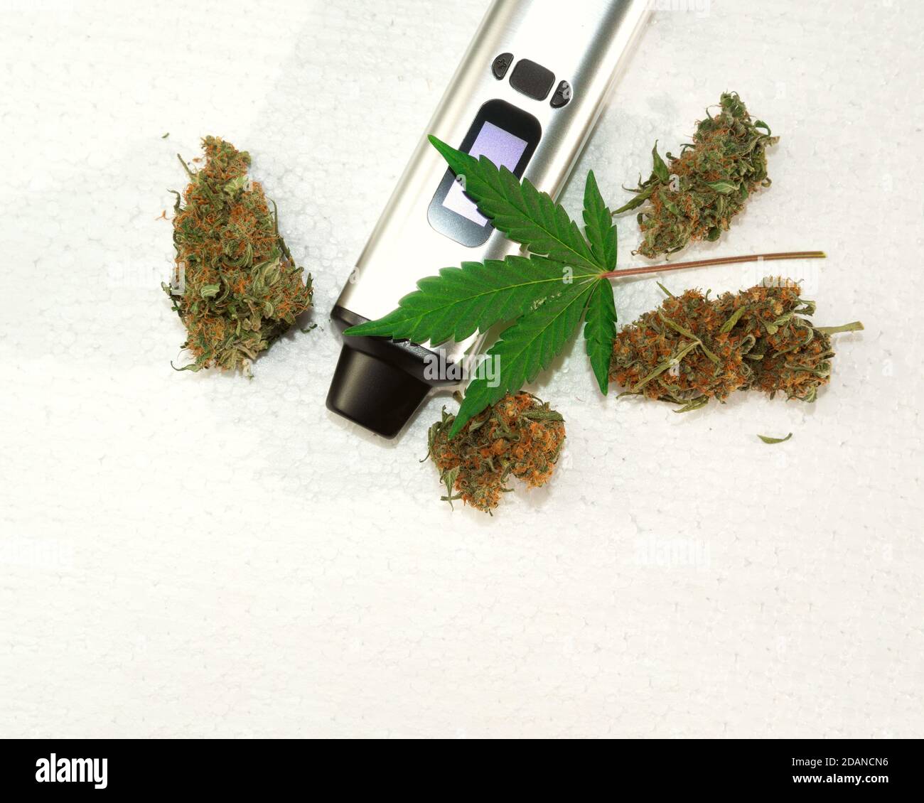 portable electronic vaporizer for smoking dry herbs next to hemp leaves Stock Photo