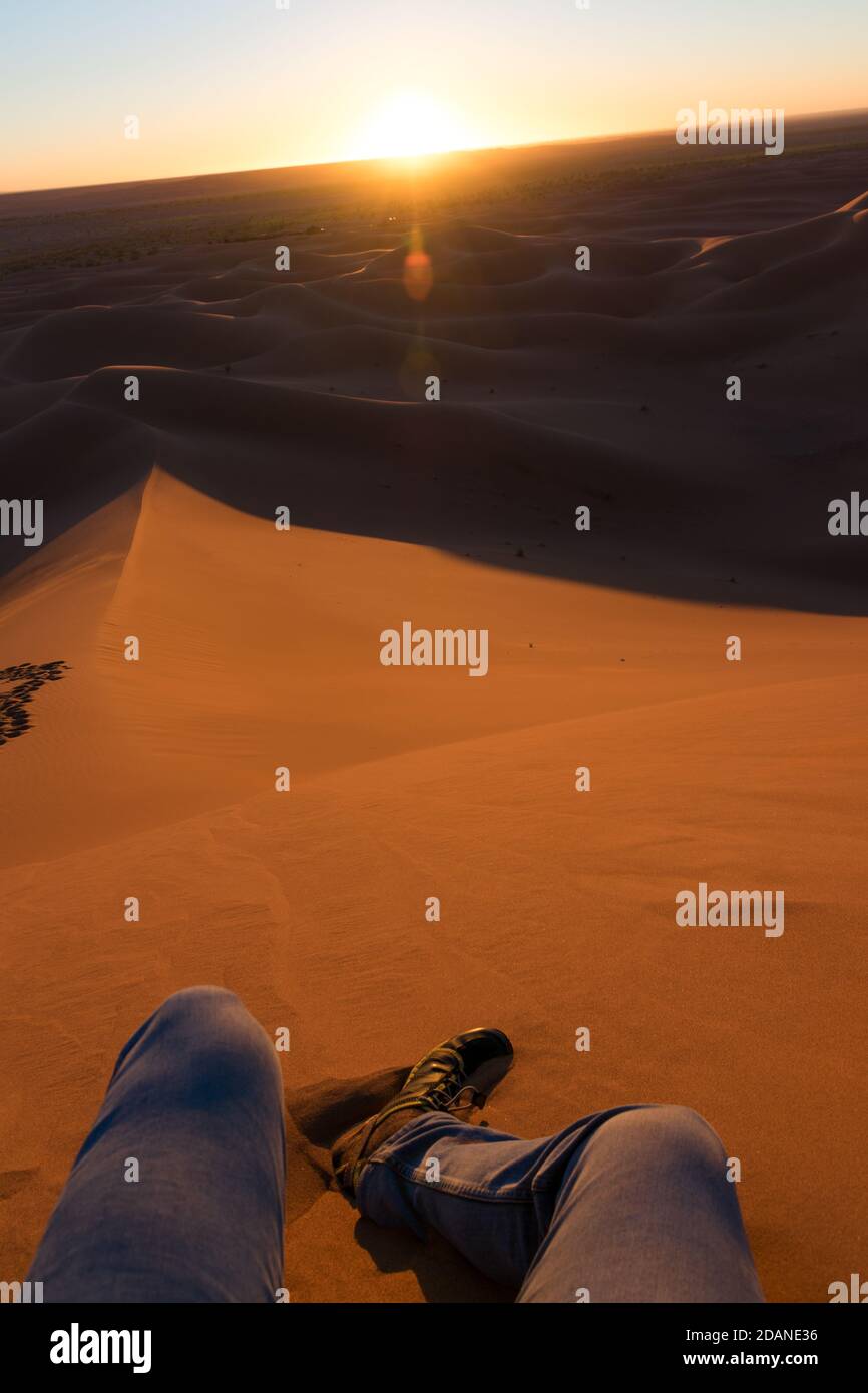 Legs of unrecognizable man from the top of a dune at sunrise, in Erg Chigaga, Morocco Stock Photo