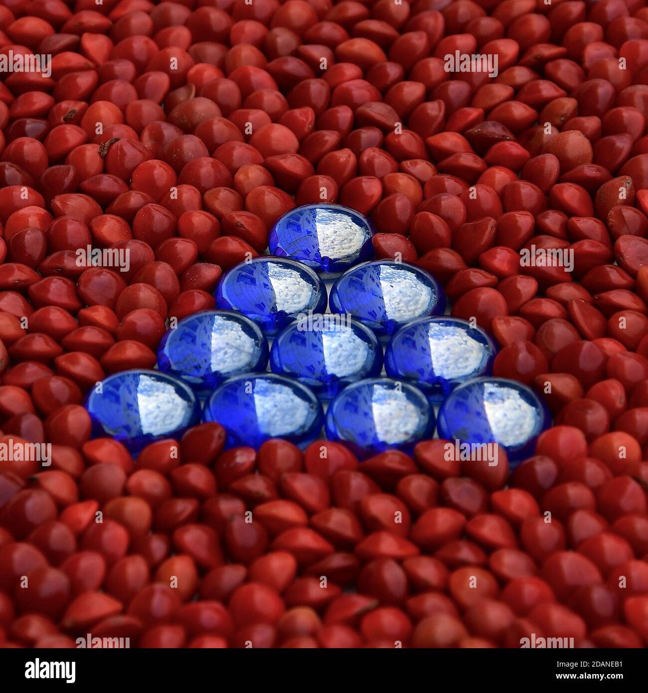 Triangle of blue iridescent glass beads isolated on a background of shiny red beads. Stock Photo