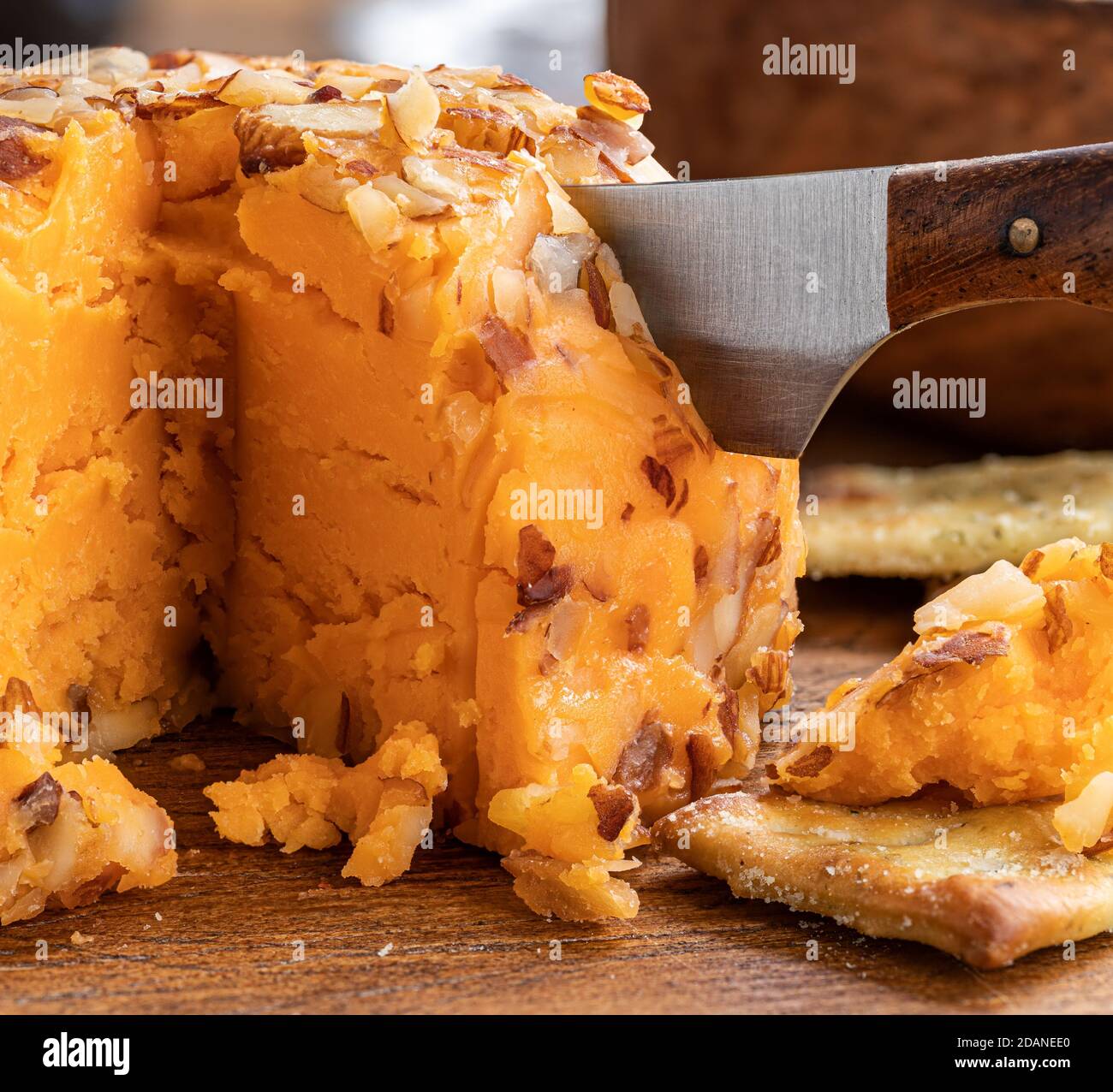 Closeup of a cheddar cheese ball cut by a knife and crackers on a wooden surface Stock Photo