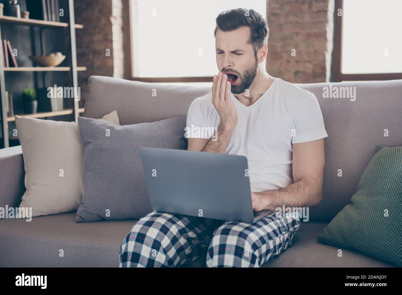 Photo of exhausted man sit divan work remote laptop tired prepare startup progress innovation report yawn mouth hand wear sleepwear nightwear in house Stock Photo Alamy