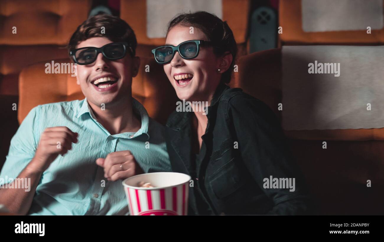 Man and woman in the cinema watching a movie with 3D glasses. with interest looking at the screen, exciting and eating popcorn Stock Photo