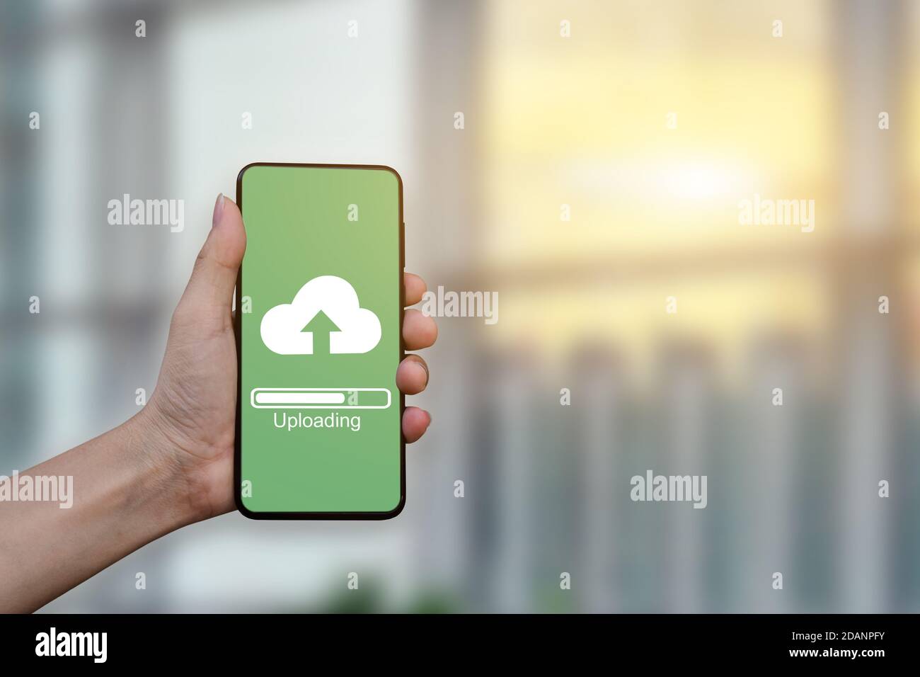 Close up of hand holding mobile smartphone with cloud upload to store data on server. Stock Photo